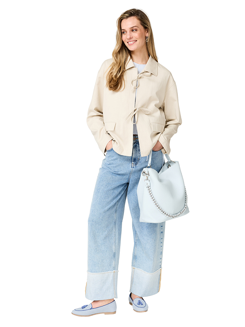 Modieuze voorjaarss outfit met een beige jas, wijde jeans, lichtblauwe loafers en lichtblauwe handtas tegen een witte achtergrond.