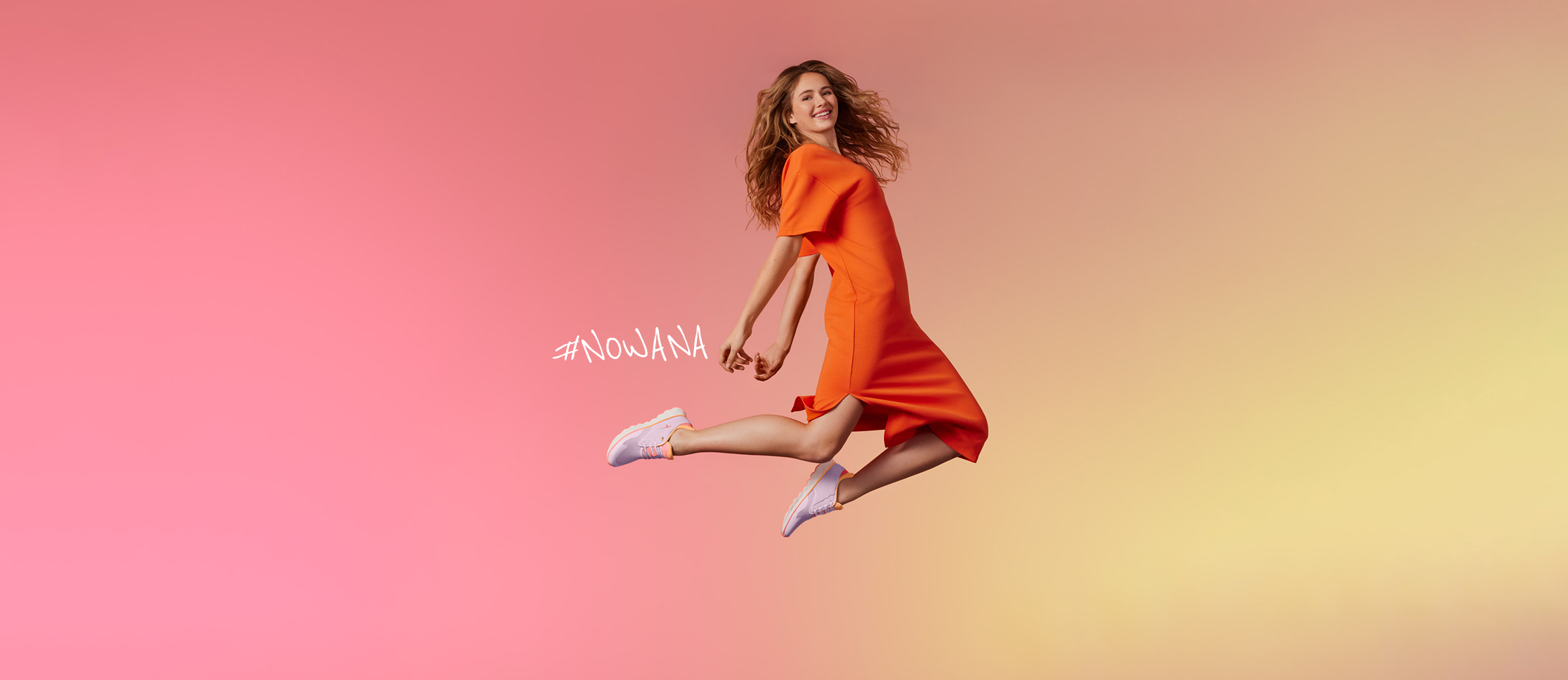 Dynamic shot of a woman in an orange dress jumping in front of a pink and yellow background, wearing white sneakers and the text #NOWANA