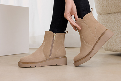 Beige suede ankle boots with gold zip and beige sole, worn with black jeans.