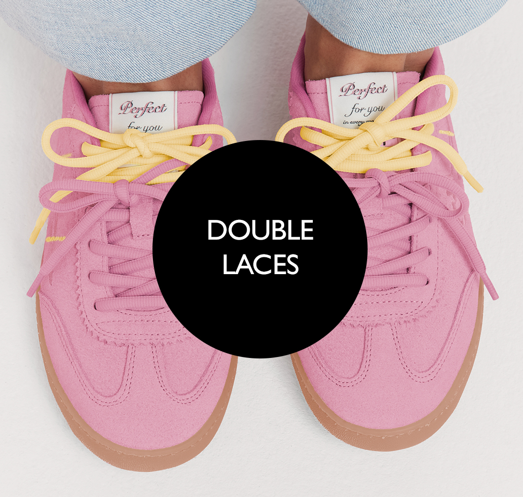 Pink trainer with double lacing in pink and yellow on a white background, with a brown rubber sole.
