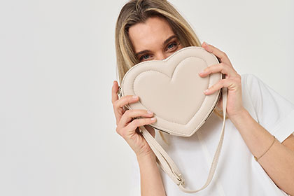 Una donna in abbigliamento bianco mostra una borsa beige a forma di cuore.