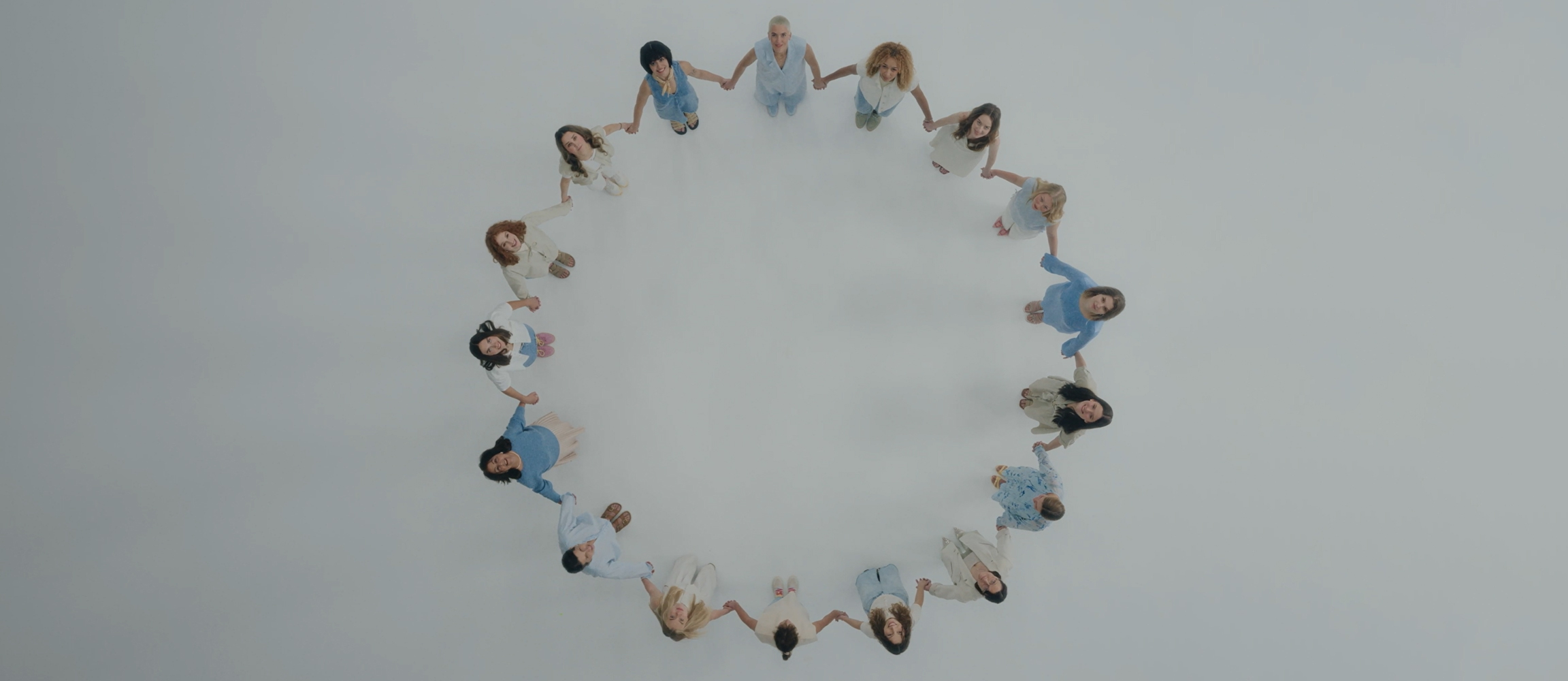 A group of people in light blue and white clothing, photographed spirally from above, forming a circular pattern on a light background.
