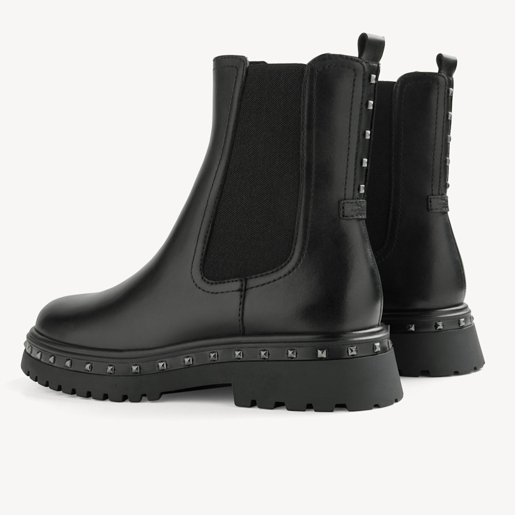Chelsea boots noires avec empiècement élastique, ornement clouté sur la semelle et profil robuste sur fond blanc.