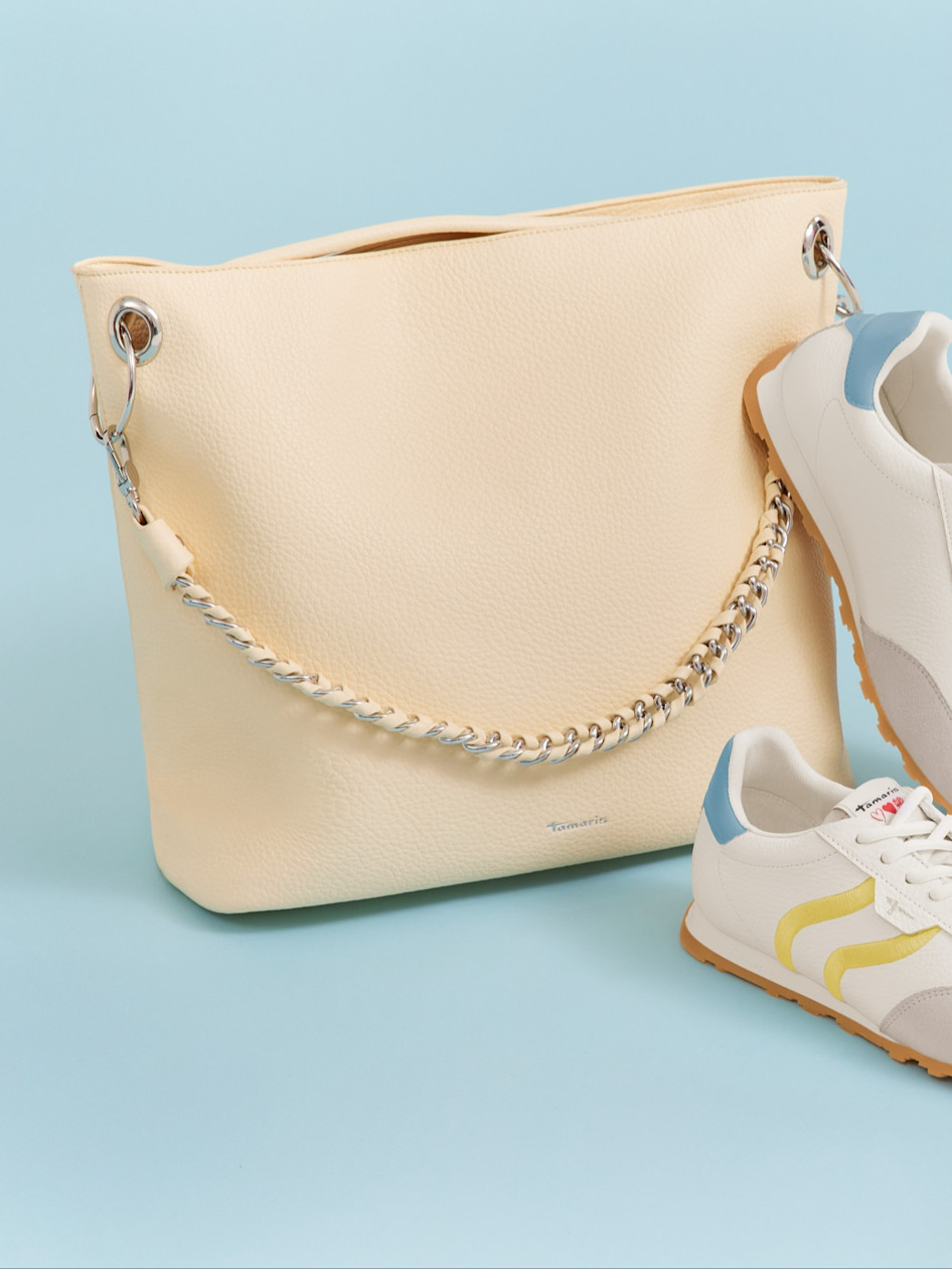 Sac &agrave; main cr&egrave;me avec cha&icirc;ne en argent &agrave; c&ocirc;t&eacute; D'une Sneaker blanche avec des accents jaunes et bleus sur fond bleu clair