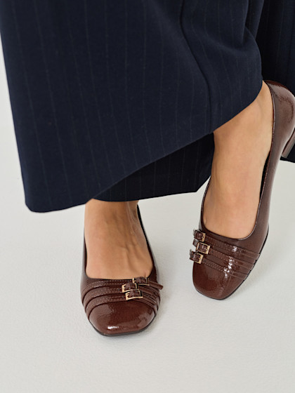 Elegant brown patent leather shoes with buckles, worn with dark trousers.