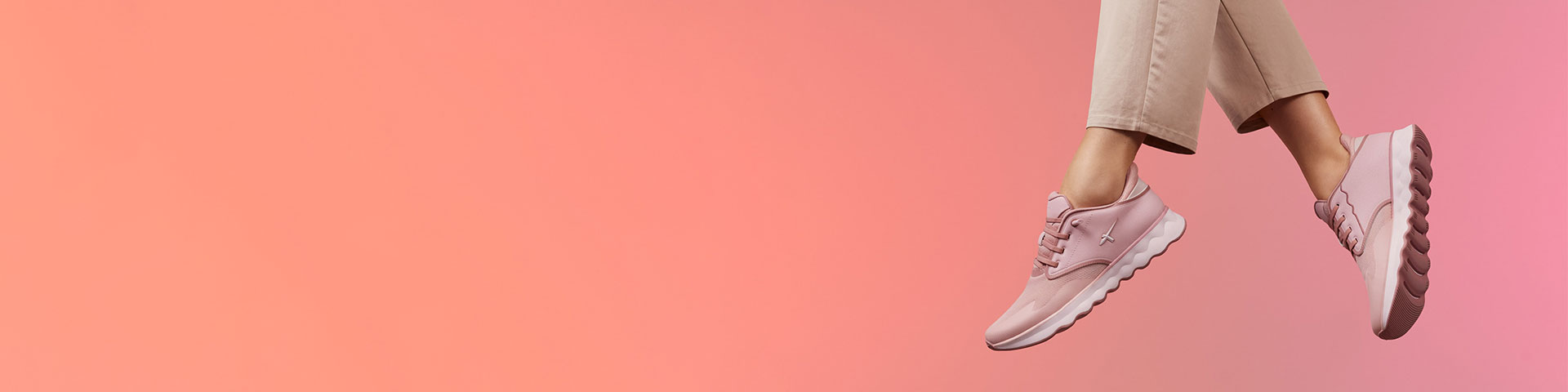 Pink sneakers and beige trousers against a coral background, dynamic movement of the feet as when jumping or dancing.