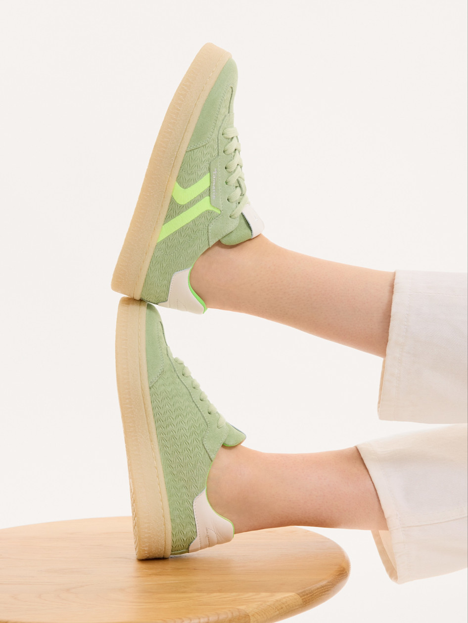 Sneaker Vert menthe avec des accents vert fluo et une semelle beige, port&eacute;e avec des chaussettes blanches sur une surface en bois.