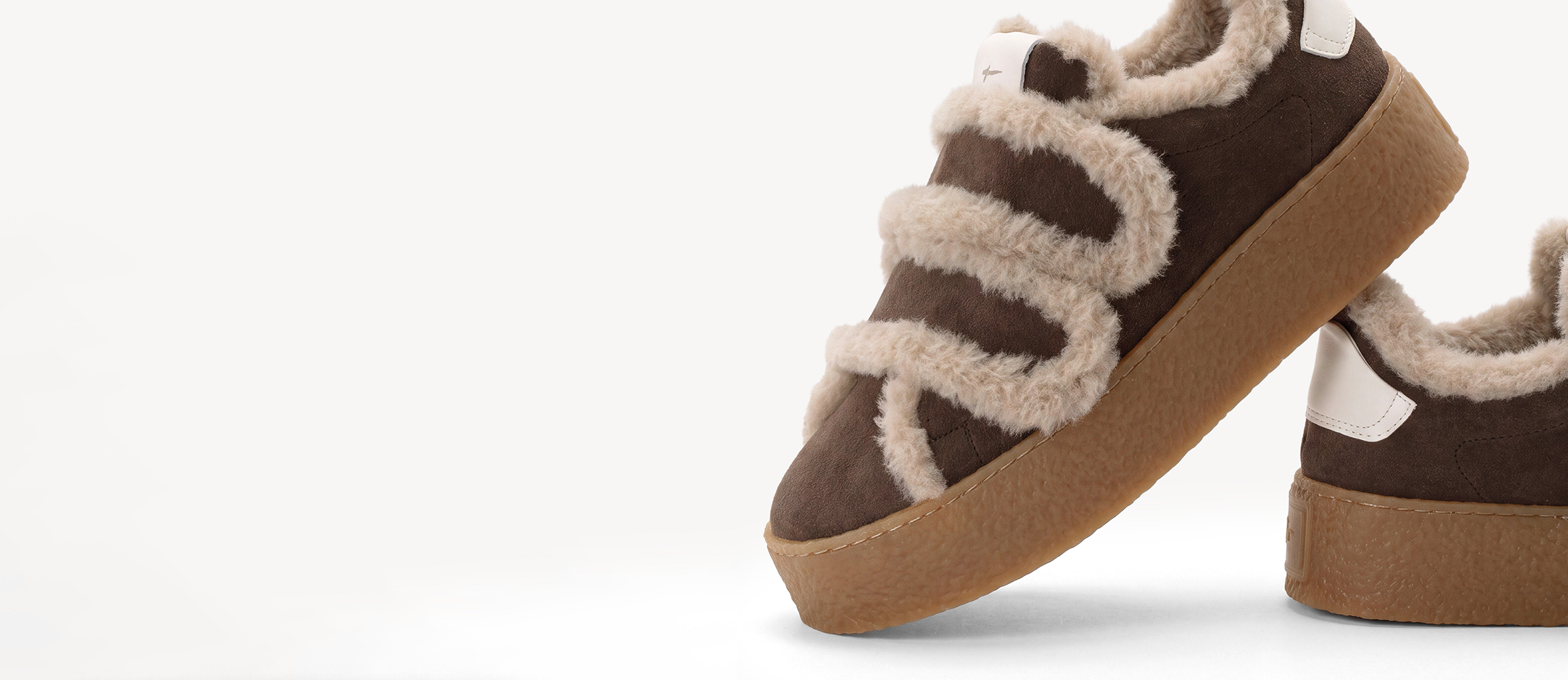 Braune Sneaker aus Wildleder mit beigen Fellverzierungen und dicker Gummisohle, Nahaufnahme auf wei&szlig;em Hintergrund.