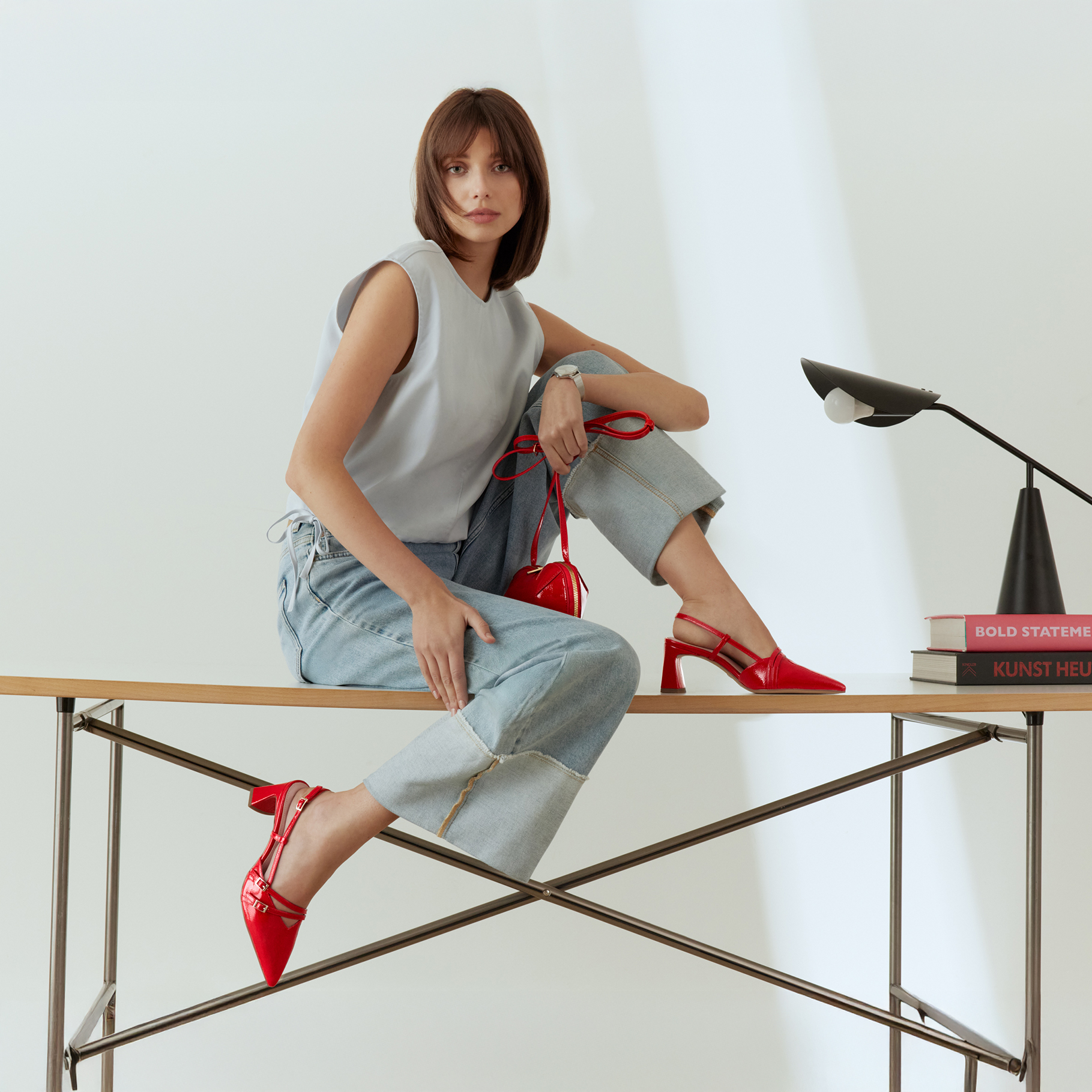 Fashionable outfit with blue top, jeans and red accessories - stylish photo shoot on a desk with minimalist design