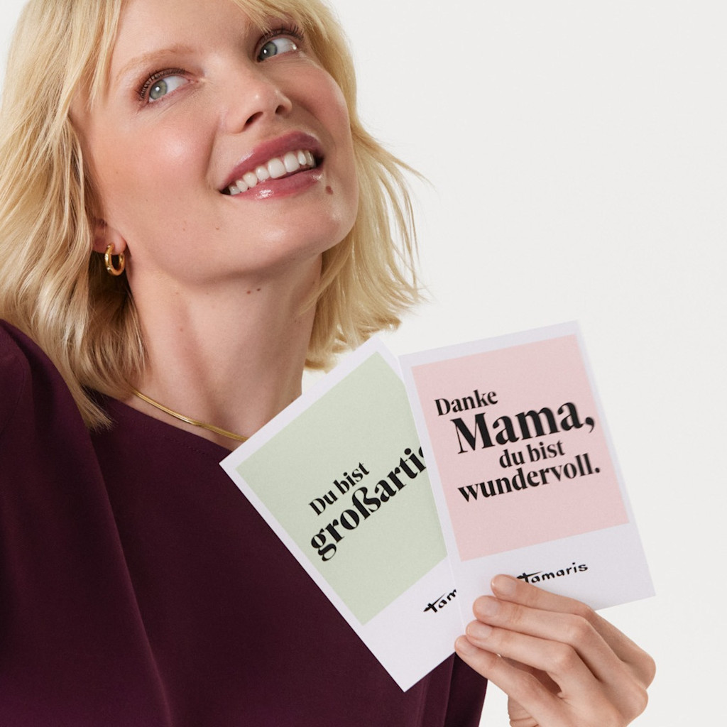 Lächelnde Frau in bordeauxrotem Pullover hält Grußkarten mit Aufschriften "Du bist großartig" und "Danke Mama, du bist wundervoll"