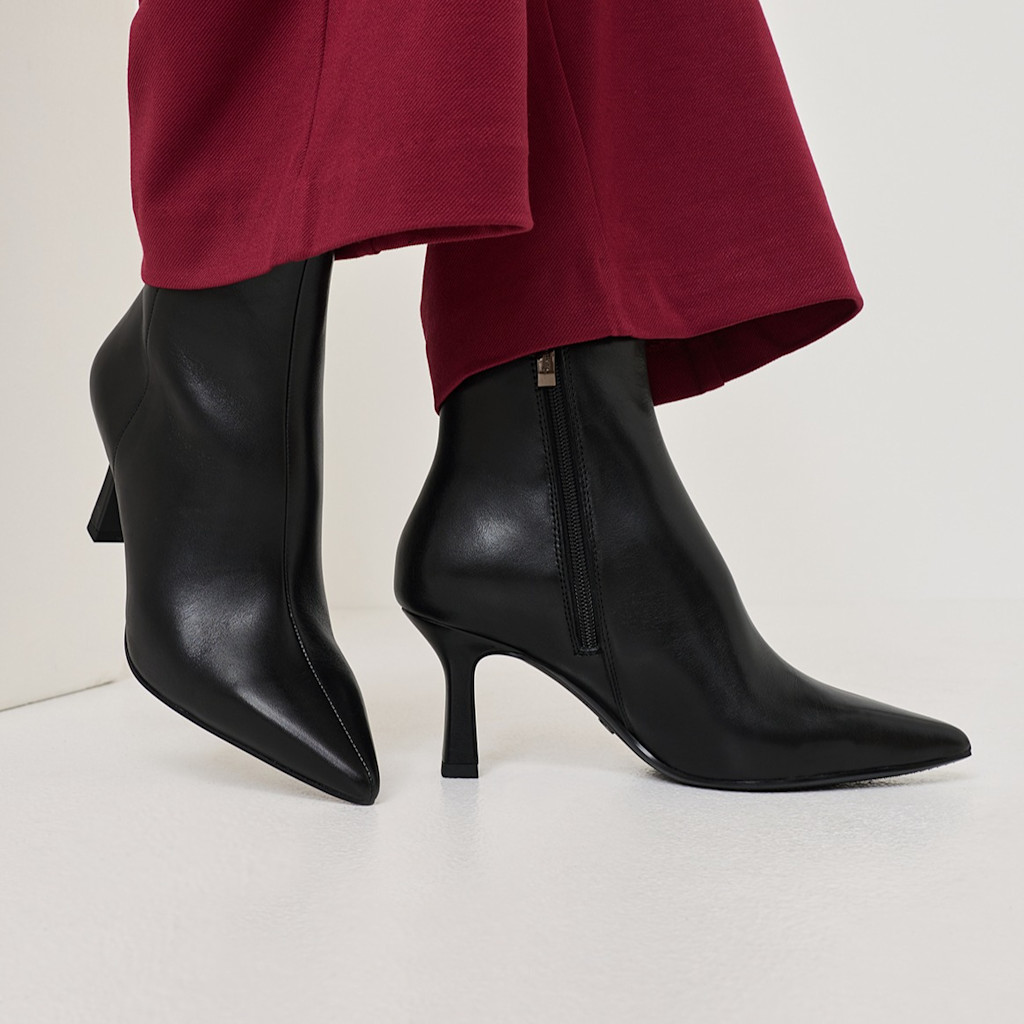 Elegant black leather boots with a narrow heel, worn with wine-red trousers against a white background.