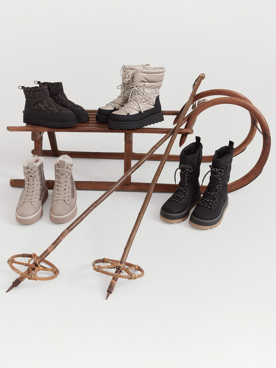 Winterstiefel in Schwarz und Beige auf und vor einem vintage Holzschlitten