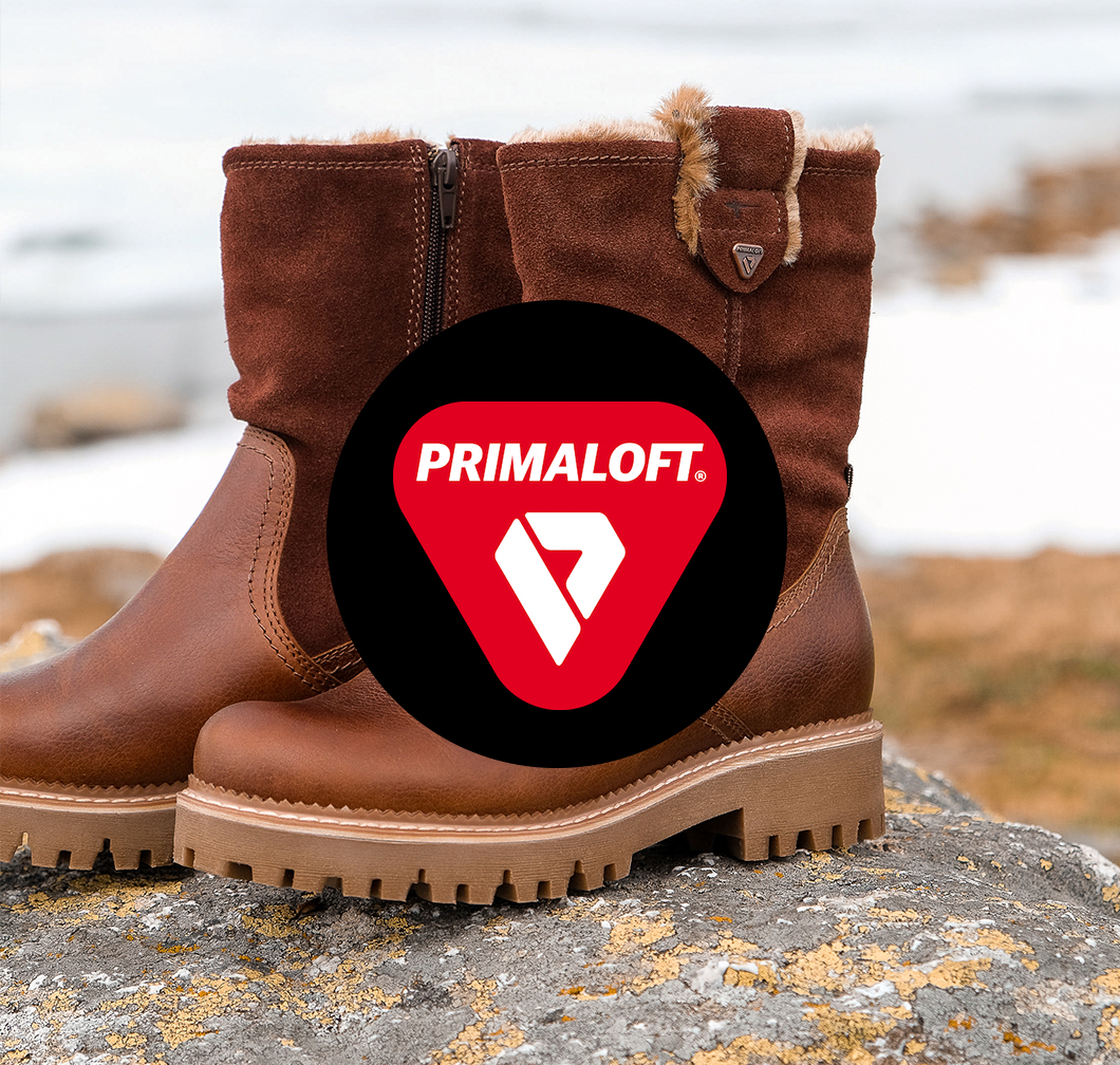 Braune Winterstiefel aus Wildleder mit Primaloft-Isolierung, Fellbesatz und robuster Profilsohle auf felsigem Untergrund.