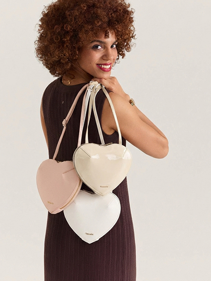 Une femme en robe sombre porte trois sacs &agrave; main cr&egrave;me en forme de c&oelig;ur, suspendus &agrave; des bandouli&egrave;res.