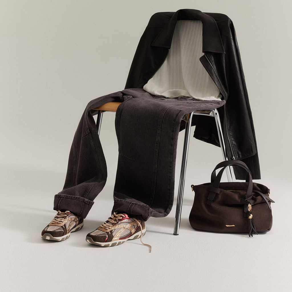 Sedia con blazer nero, jeans grigi e top bianco. Davanti, sneakers marroni e una borsa marrone scuro.