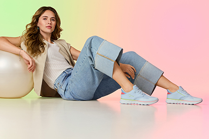 En person i jeans ligger avslappnat p&aring; golvet, b&auml;r pastellf&auml;rgade sneakers och omges av f&auml;rgat ljus.