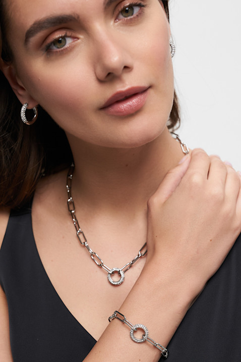 Närbild på ett silverhalsband och armband med kristallutsmyckning på en svart topp.