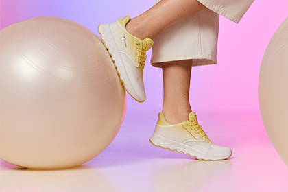Wei&szlig;e Sneaker mit gelben Details auf rosa-violettem Hintergrund mit gro&szlig;en perlmuttfarbenen Luftballons als dekorative Elemente