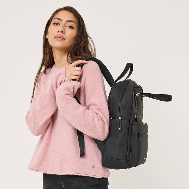 Giovane donna con maglione rosa che trasporta uno zaino in pelle nera su sfondo bianco