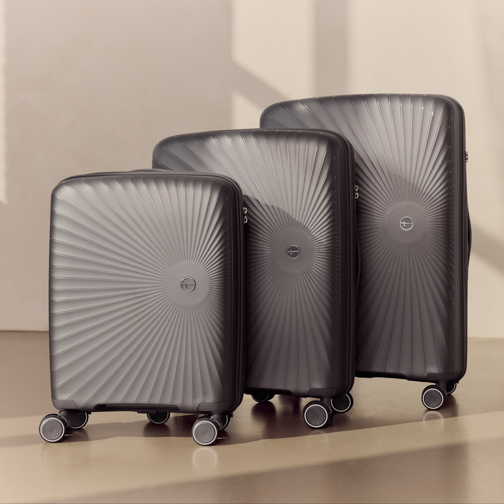 Trois valises rigides gris fonc&eacute; de diff&eacute;rentes tailles avec motif rayonnant et roulettes, sur fond clair.