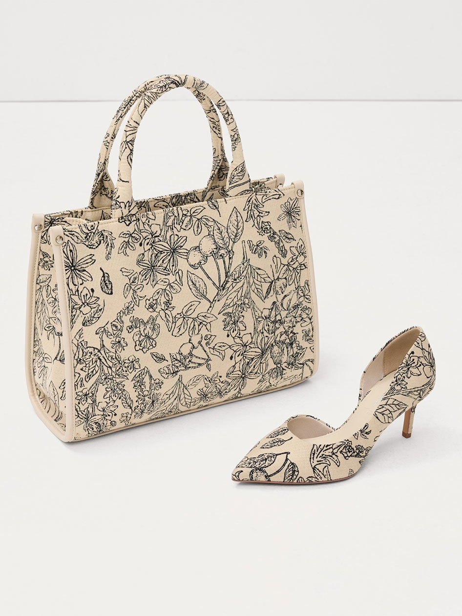 Beige h&aring;ndtaske og matchende pumps med sort blomsterm&oslash;nster, et elegant s&aelig;t p&aring; hvid baggrund.