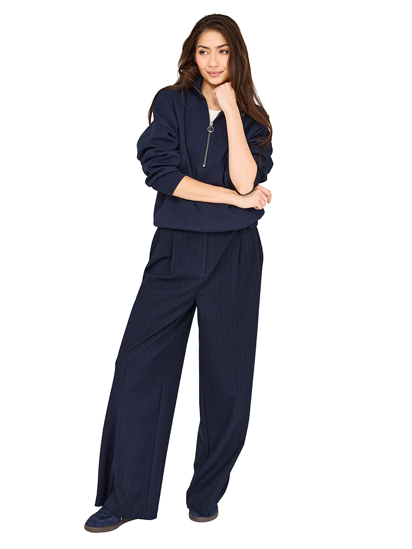 Modell in lässigem marineblauem Reißverschluss-Pullover und weiter Hose vor weißem Hintergrund.