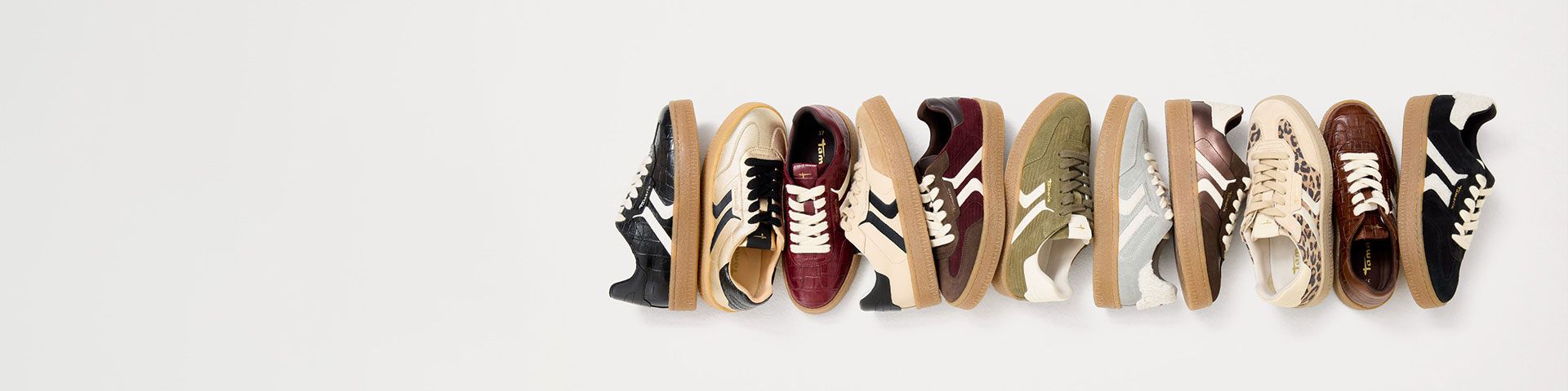 Una gamma di sneakers con suola in gomma in vari colori come nero, beige, bordeaux e verde oliva, tutte decorate con strisce bianche.