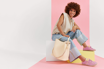 A smiling woman in jeans and a beige vest poses on colorful pedestals against a pink background.