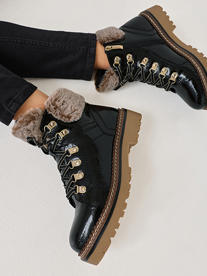 Schwarze Winterstiefel mit Fellbesatz und goldenen Schnürösen auf beiger Sohle, getragen zu dunkler Jeans