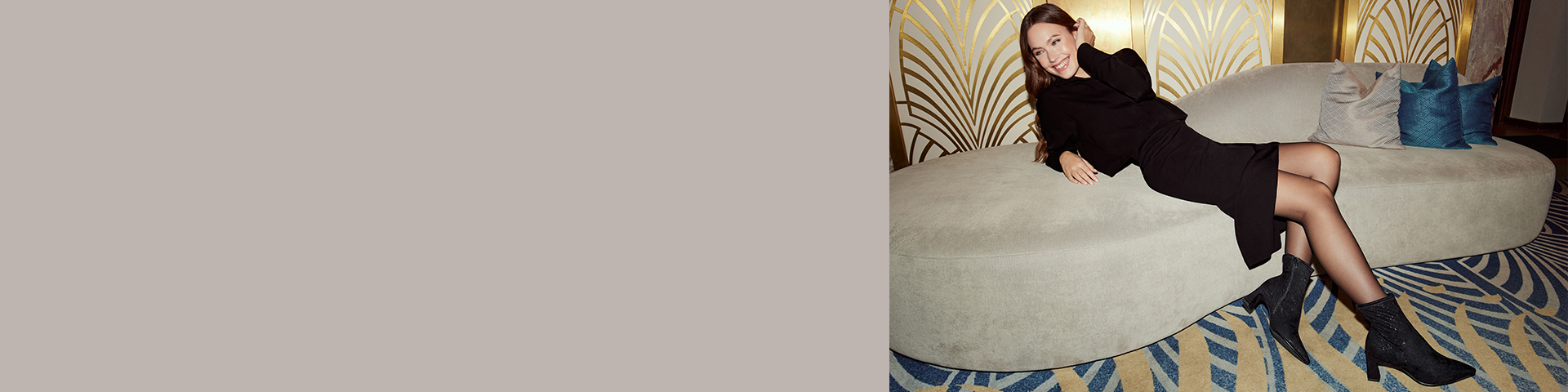 Una donna in abito nero è seduta sorridendo su un divano beige davanti a una parete Art Déco con motivo a ventaglio dorato.