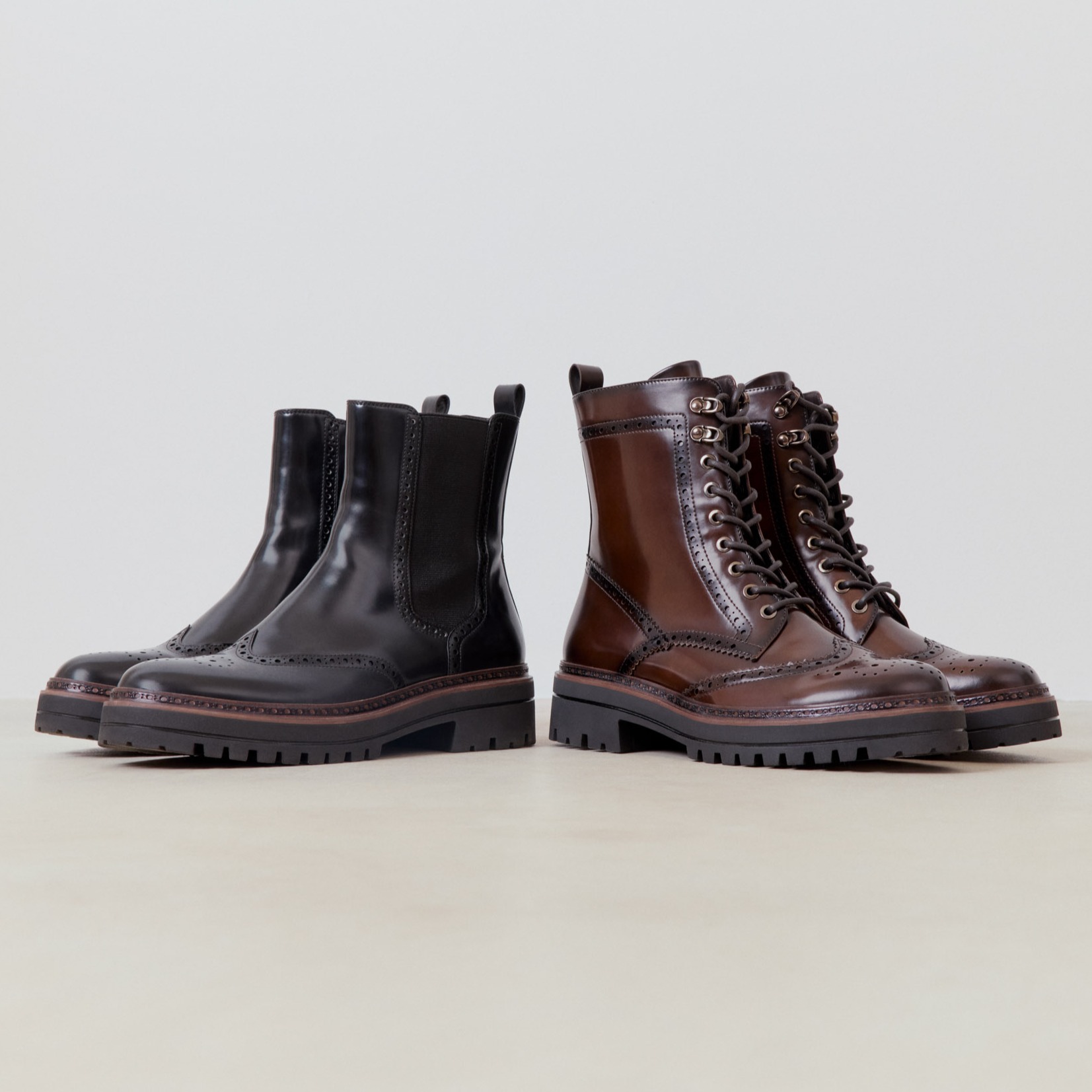 Twee elegante leren laarzen in brogue stijl: een zwarte Chelsea laars en een bruine veterlaars met een robuuste profielzool