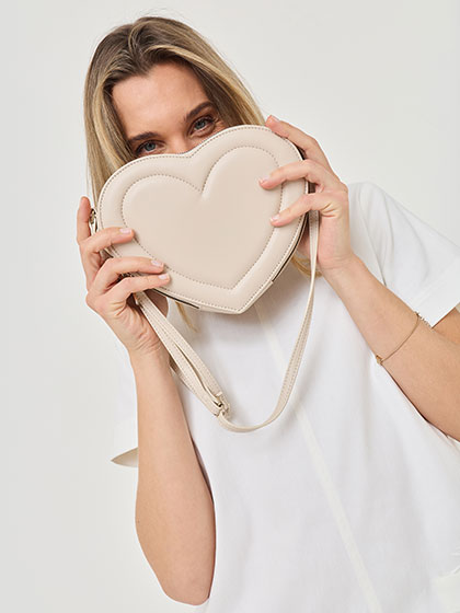 Una donna in abbigliamento bianco mostra una borsa beige a forma di cuore.