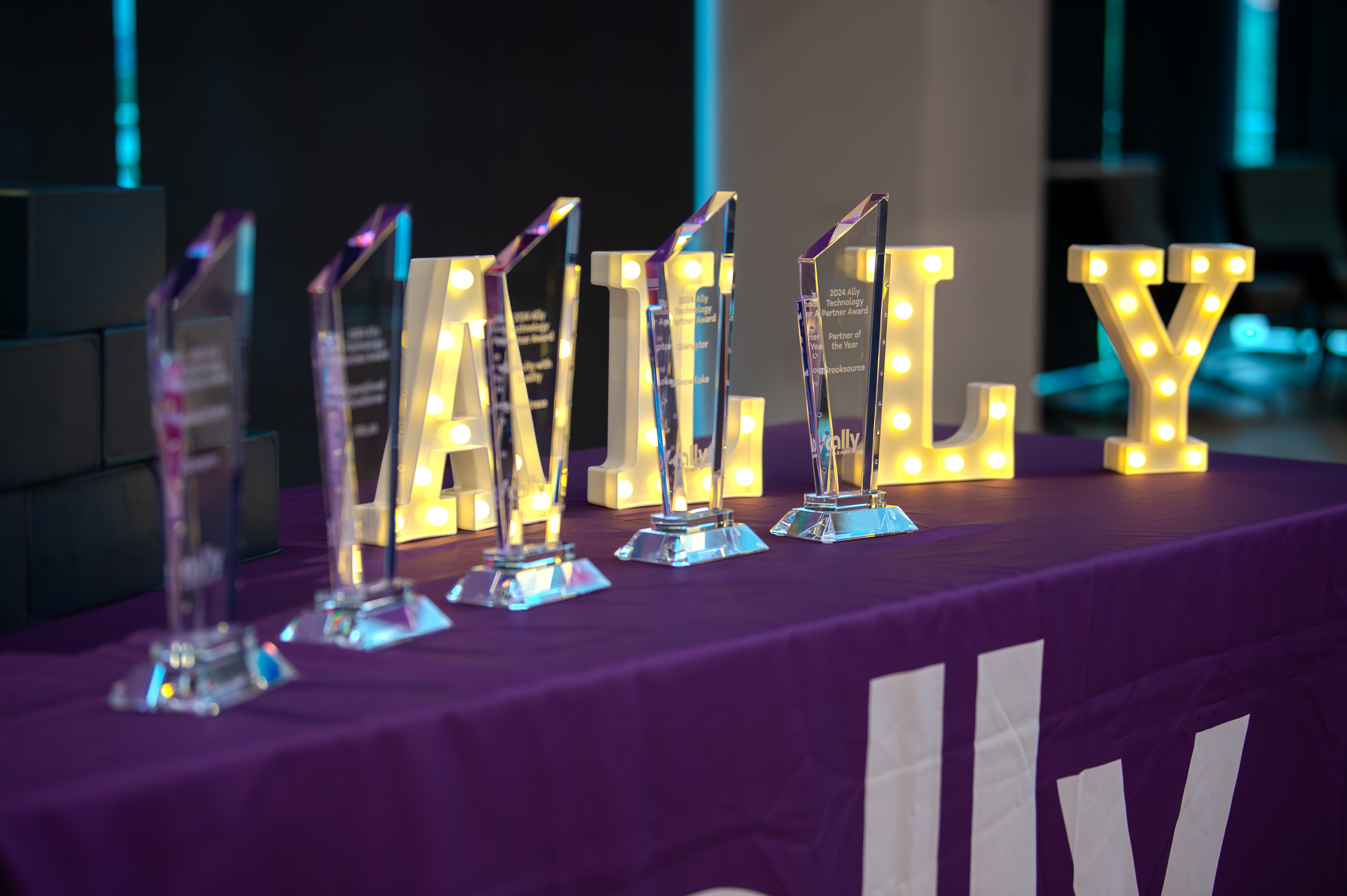Image of Ally sign lit up with award statues in front.