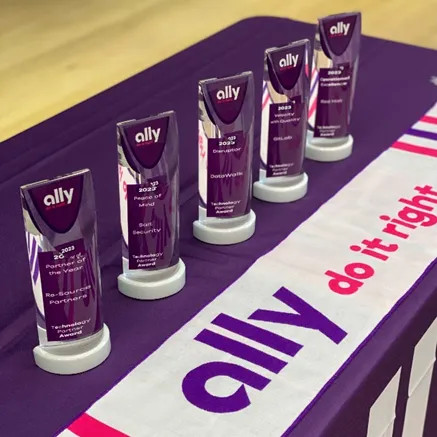 photo: Five trophies sit on a table covered with a purple Ally tablecloth and "Do it right" soccer scarf placed in front of the awards. The five categories were Operational Excellence, Peace of Mind, Velocity with Quality, Disruptor, and Partner of the Year.