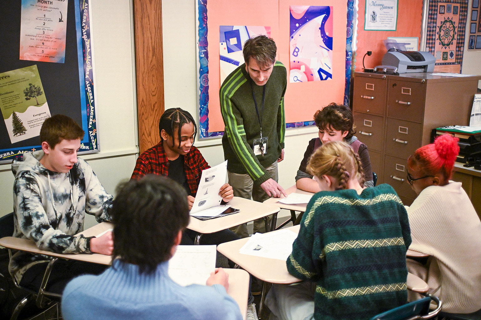 A teacher checking in with students working on a project.