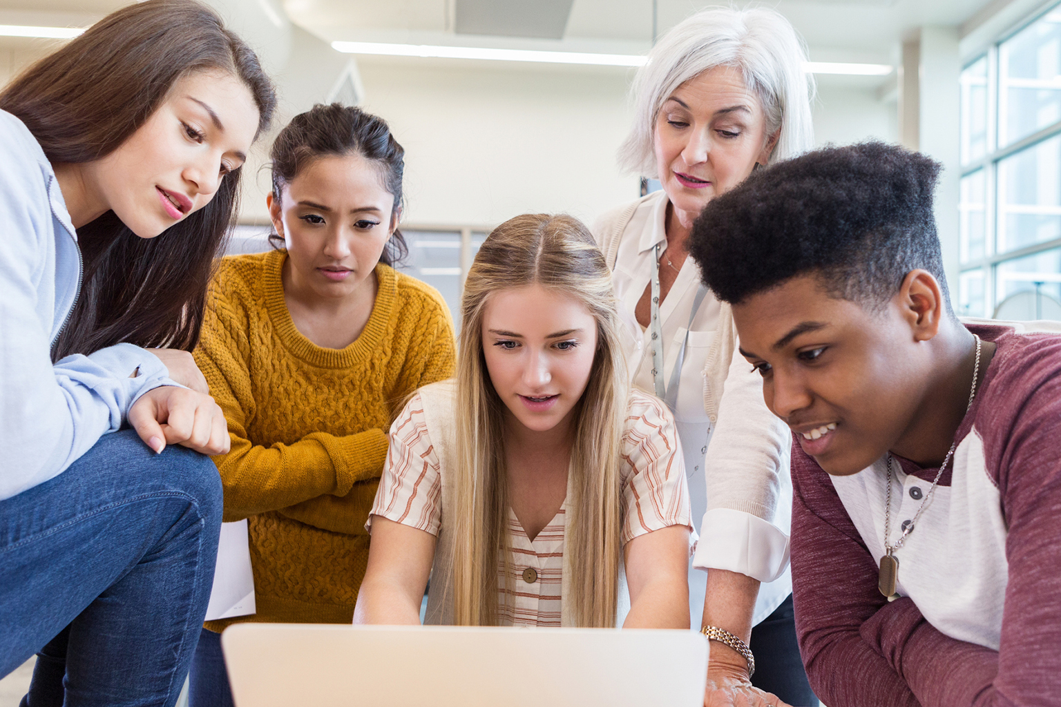A teacher and students gathered around a laptop.
