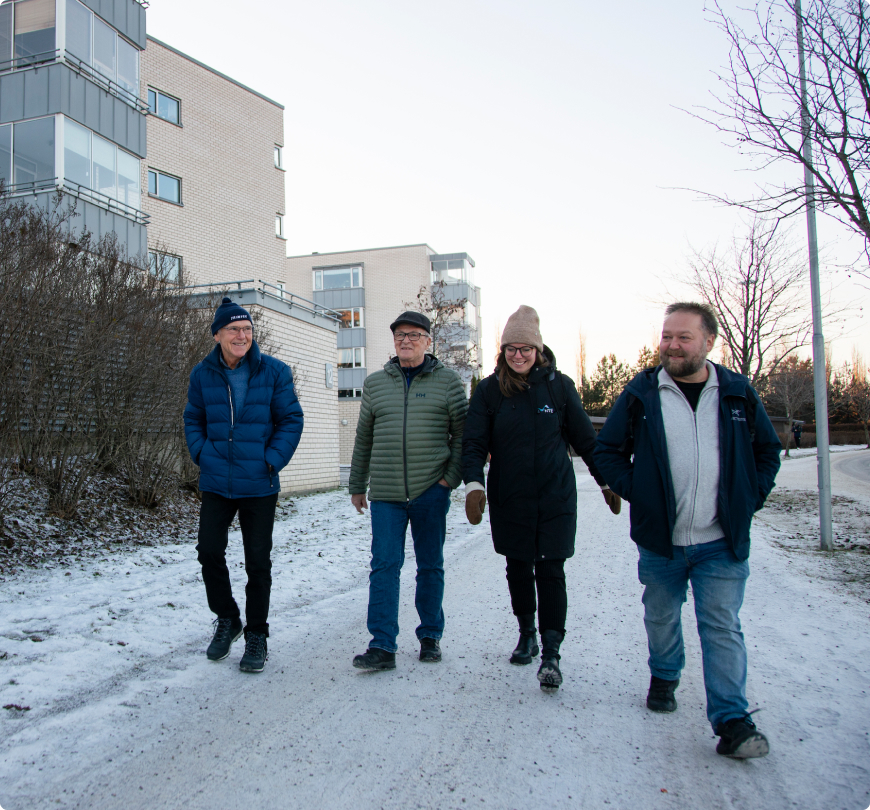 Bilde av tre menn og en kvinne som går sammen langs et fortau foran blokker i et borettslag.
