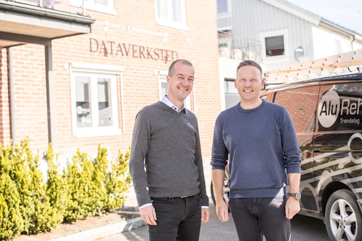 To smilende menn utenfor en bygning hvor det står dataverksted på veggen. To smilende menn utenfor en bygning hvor det står dataverksted på veggen.