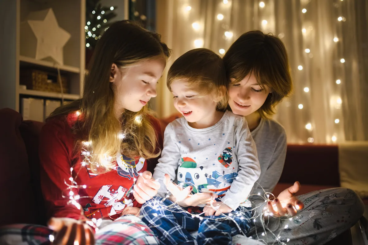 Julestemning med lyslenker Tre barn i pysj i stue med julelys