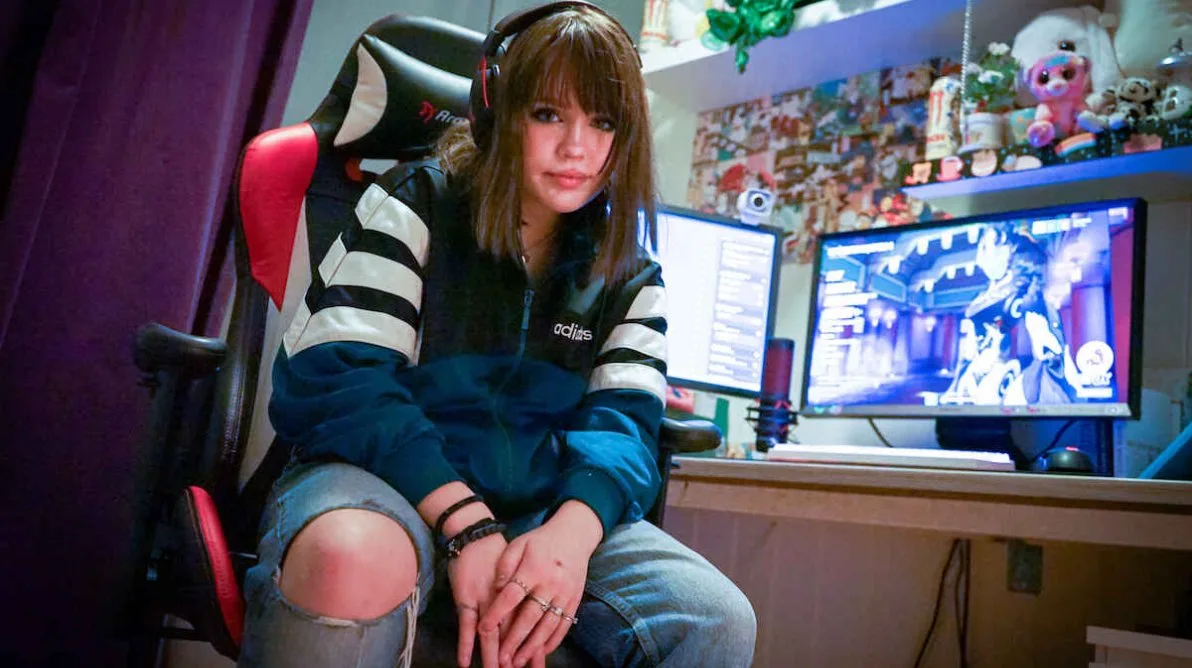 Jente med brunt hår sitter foran to PC-skjermer på jenterommet og spiller Jente med brunt hår sitter foran to PC-skjermer på jenterommet og spiller