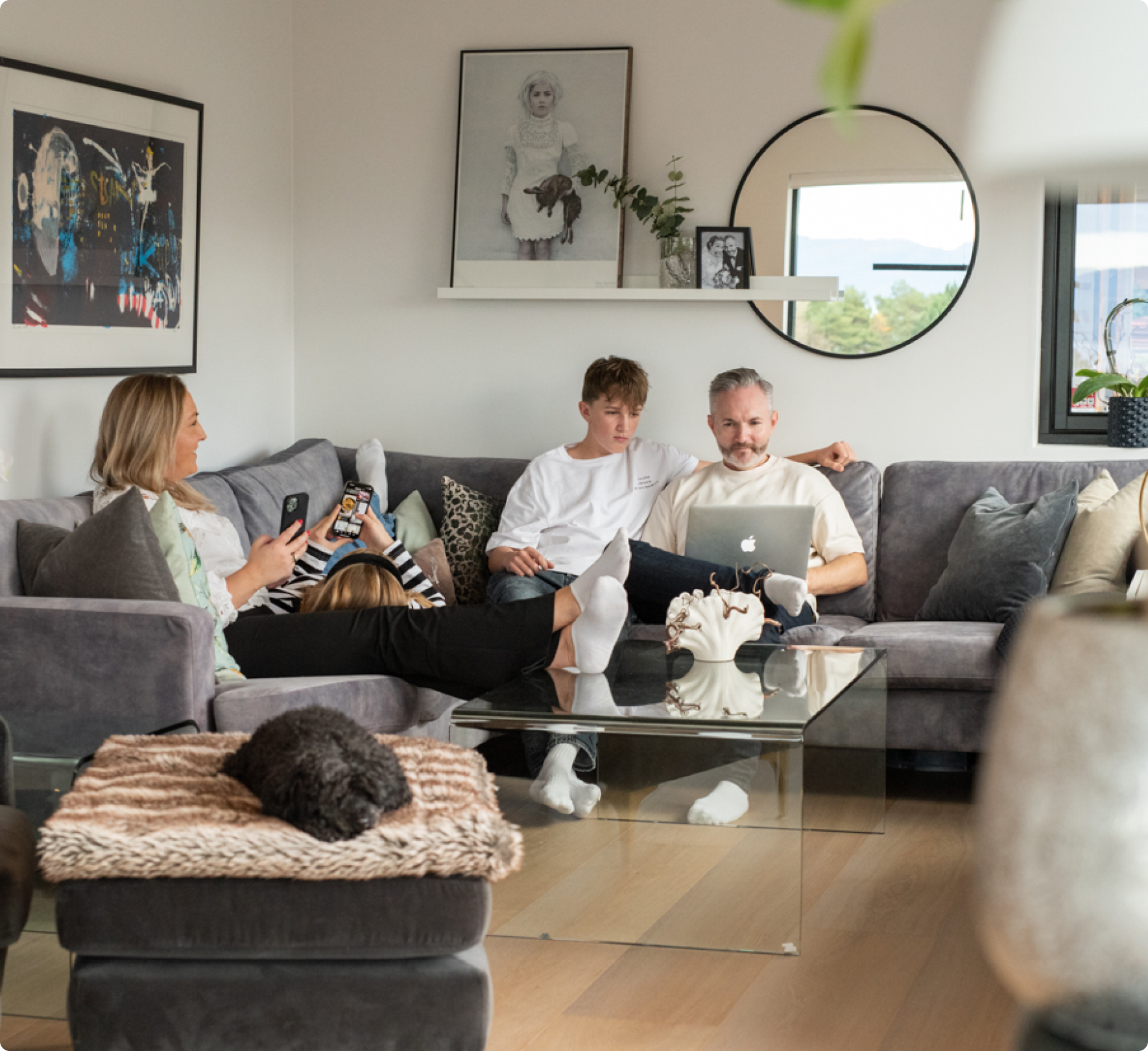 Familie som sitter i sofa i en stue med hver sin enhet