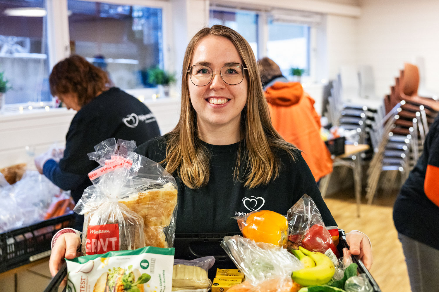 En kvinne holder fram en matkasse og smiler. Foto