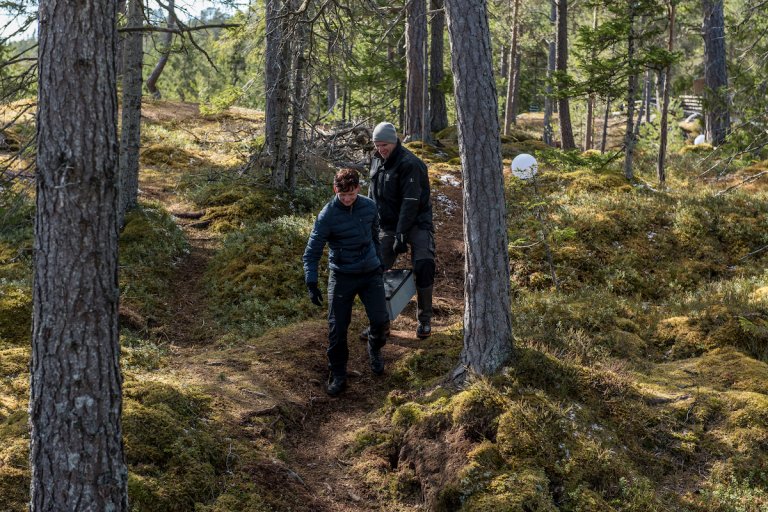 To personer bærer et stort batteri gjennom skogen
