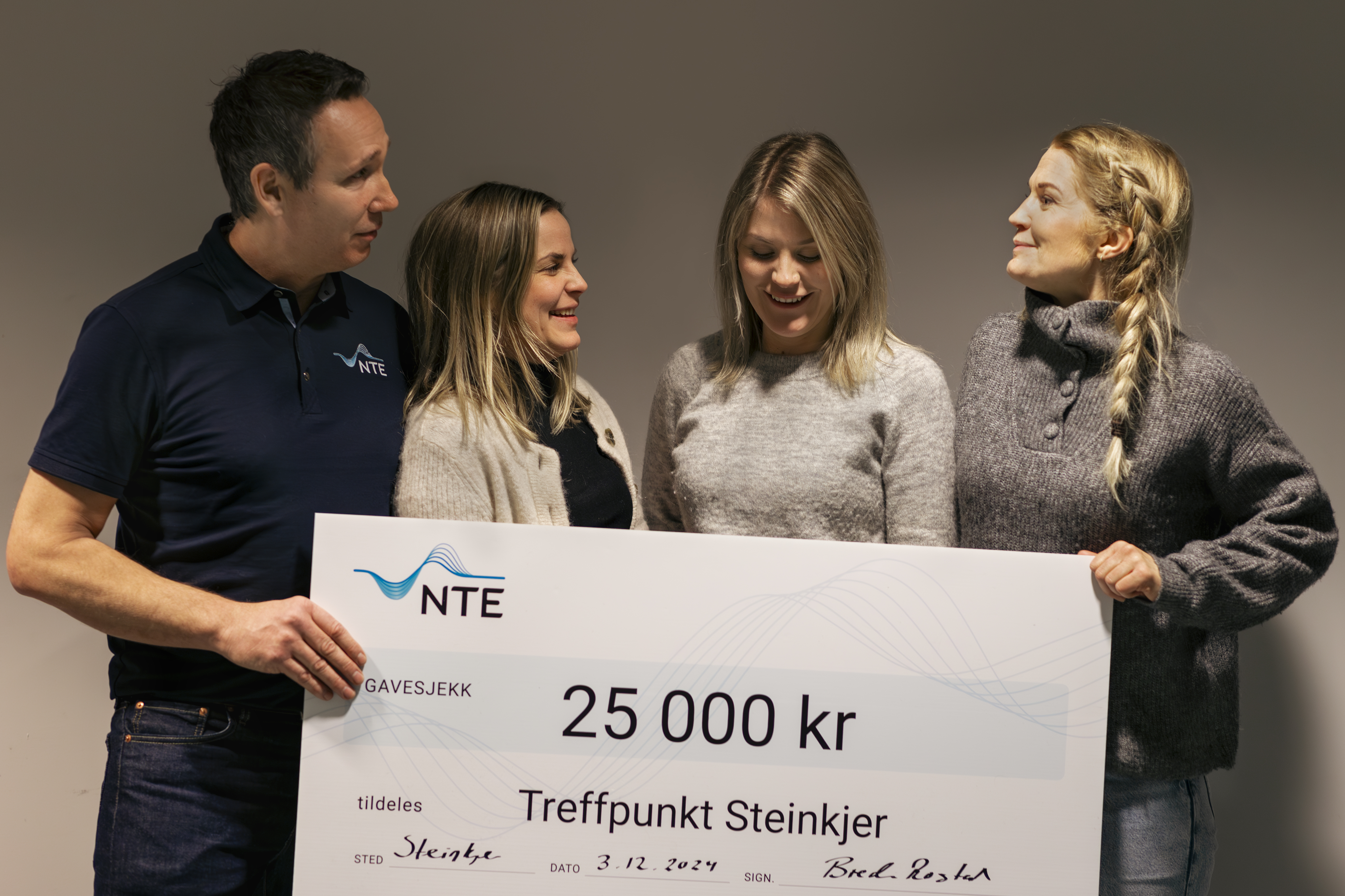 En mann og tre damer holder leende opp en sjekk på 25 000 kroner. 