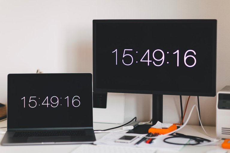 To skjermer med en skjermsparer som viser klokka