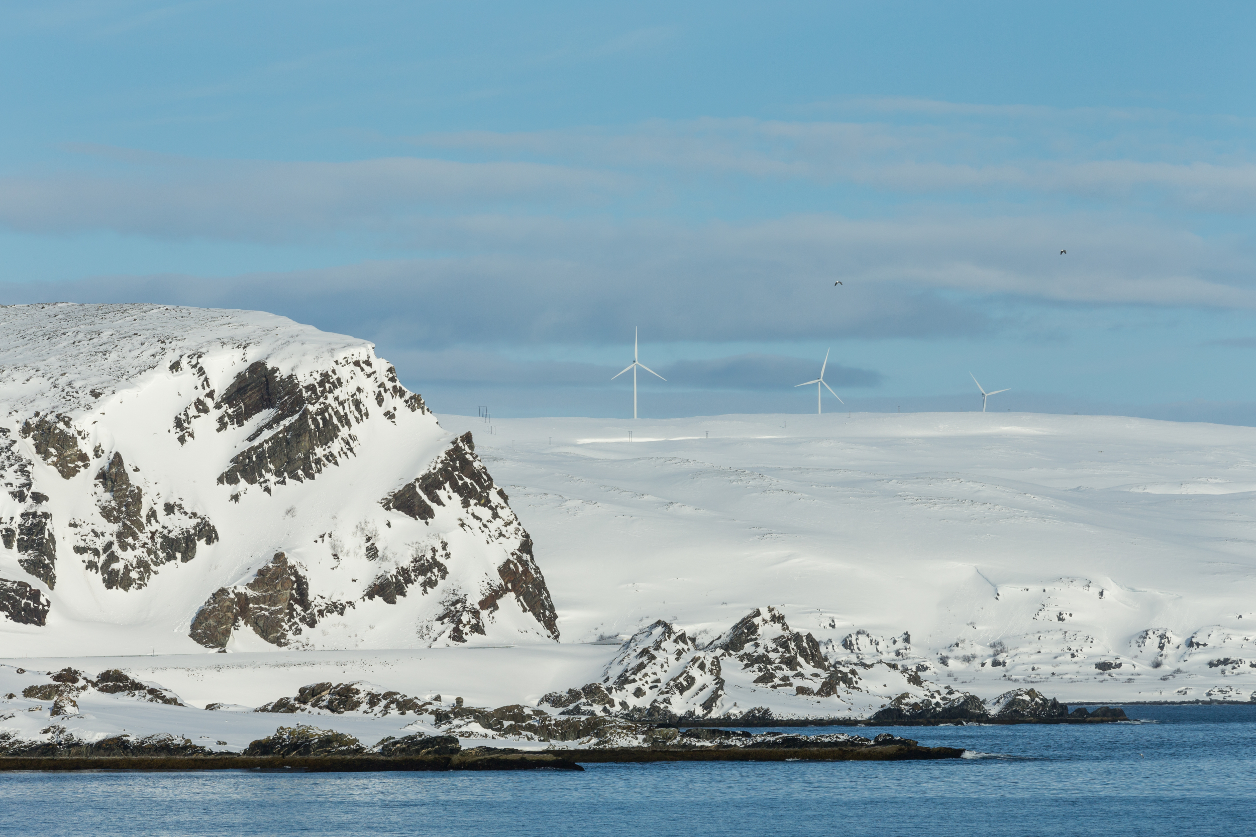 Snødekt kystlandskap med fjell og vindmøller under blå himmel