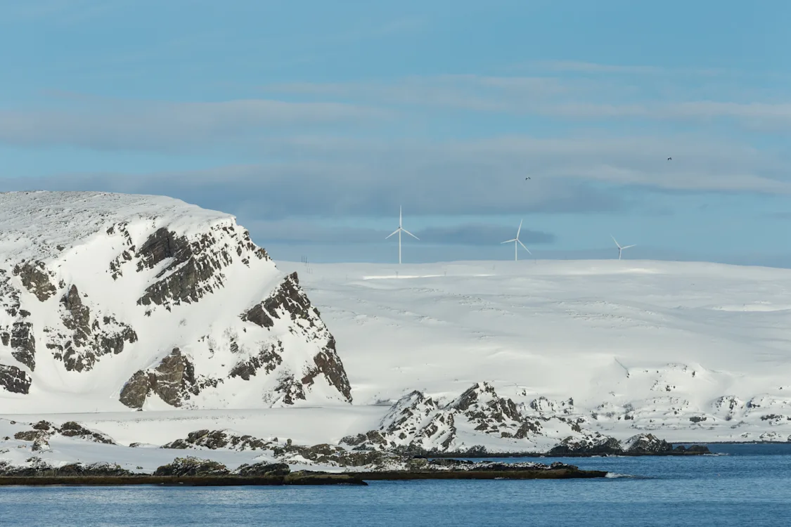 Snødekt kystlandskap med fjell og vindmøller under blå himmel Snødekt kystlandskap med fjell og vindmøller under blå himmel