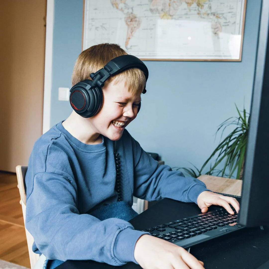 Gutt foran PC Gutt med headset sitter foran PC og gamer. Gutten smiler og er engasjert. Bilde.