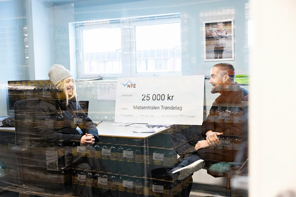 karianne brattgjerd og Jort Reitsma En mann og en kvinne i samtale. Mellom dem står en stor sjekk på 25 000 kroner til Matsentralen Trøndelag.