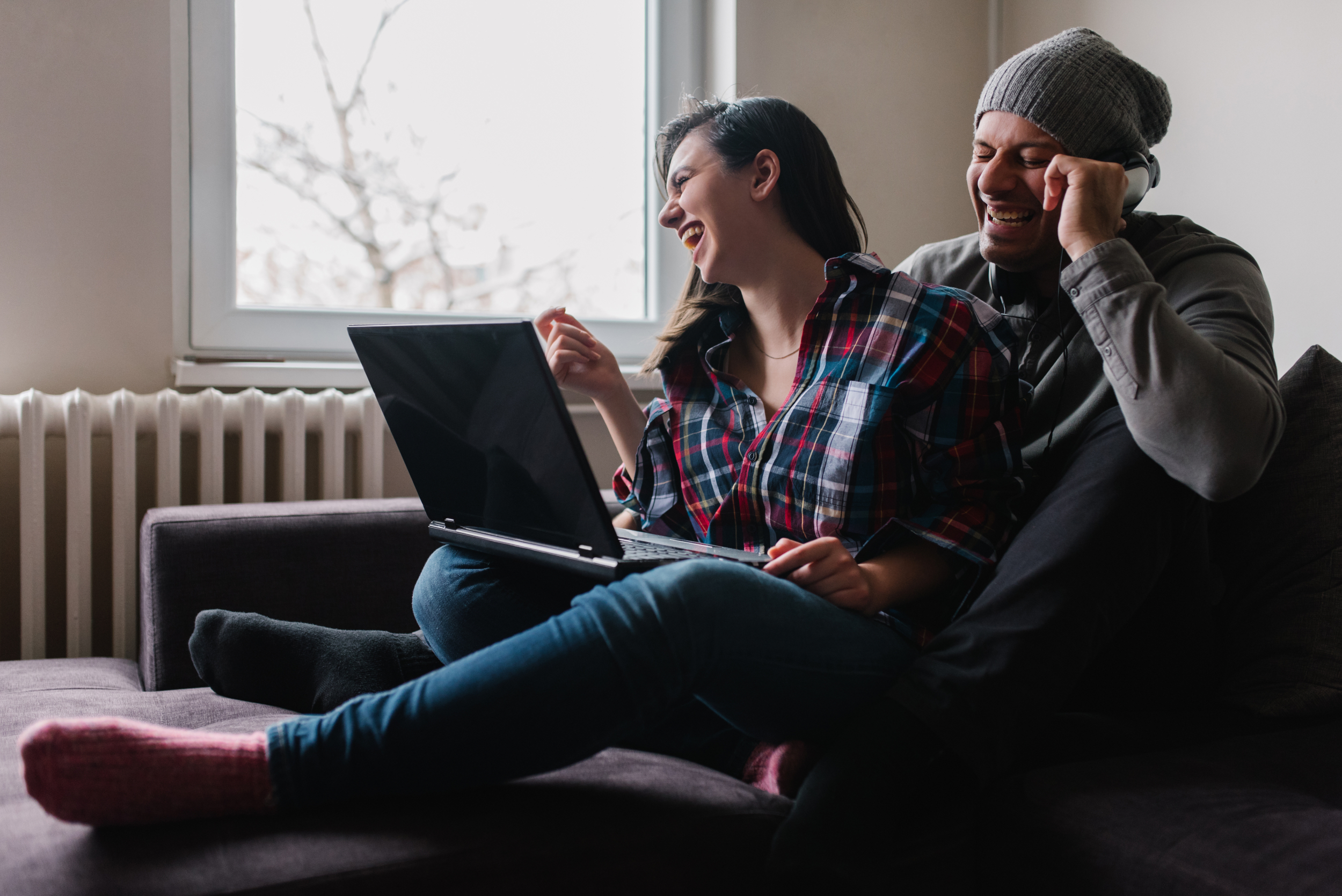 Bildet viser en kvinne og en mann som sitter i en sofa og ler med en laptop på fanget
